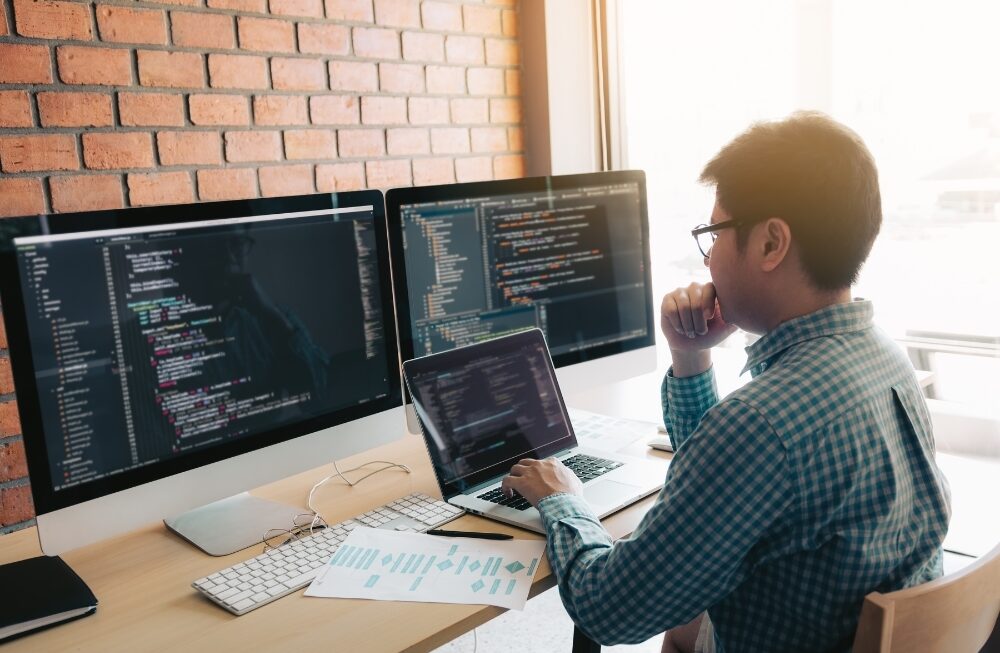 Web developer writing code on multiple screens with flowcharts and project data on the desk at website development agency in gurgaon